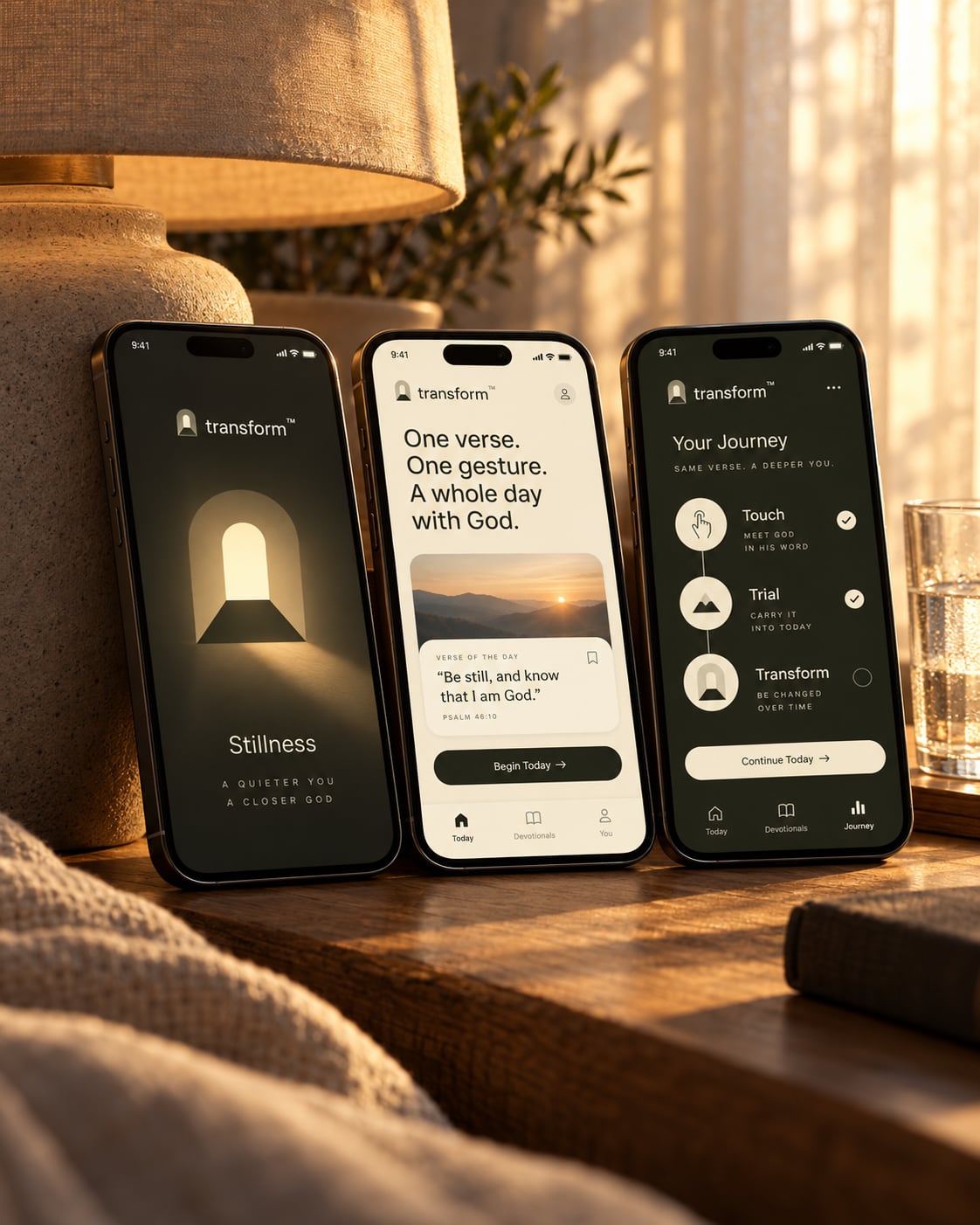 Três celulares apoiados numa mesa ao lado de um abajur mostram as telas do app devocional da Transform.